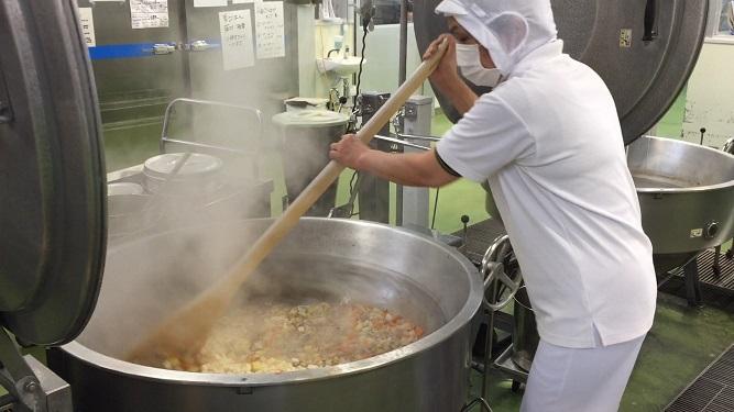 白衣の調理員が食材を大きな鍋でかき混ぜている場面を写した多良木町学校給食センターの内部写真
