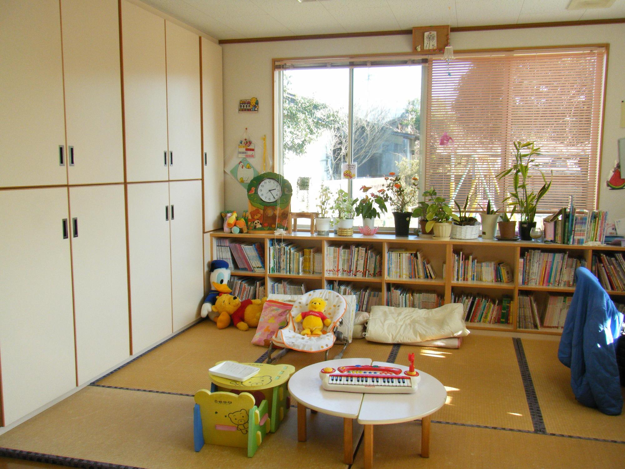 むつみ保育園子育て支援センター内観の写真。畳敷きの上にぬいぐるみなどの玩具があり、本棚には絵本が並んでいます。