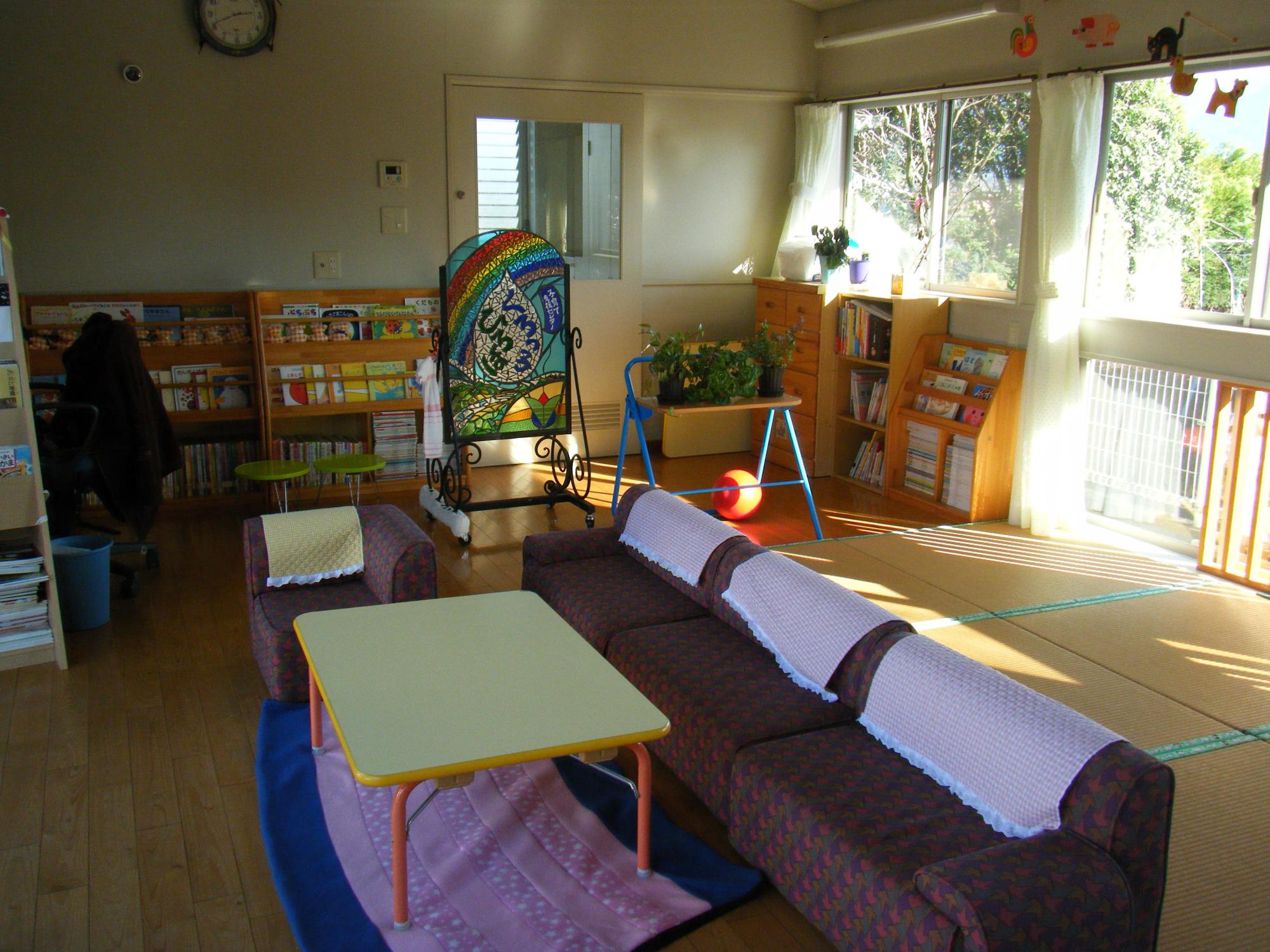 黒肥地保育園子育て支援センター内観の写真。本棚には絵本があり、中央にテーブルと広い横長のソファーがあります。