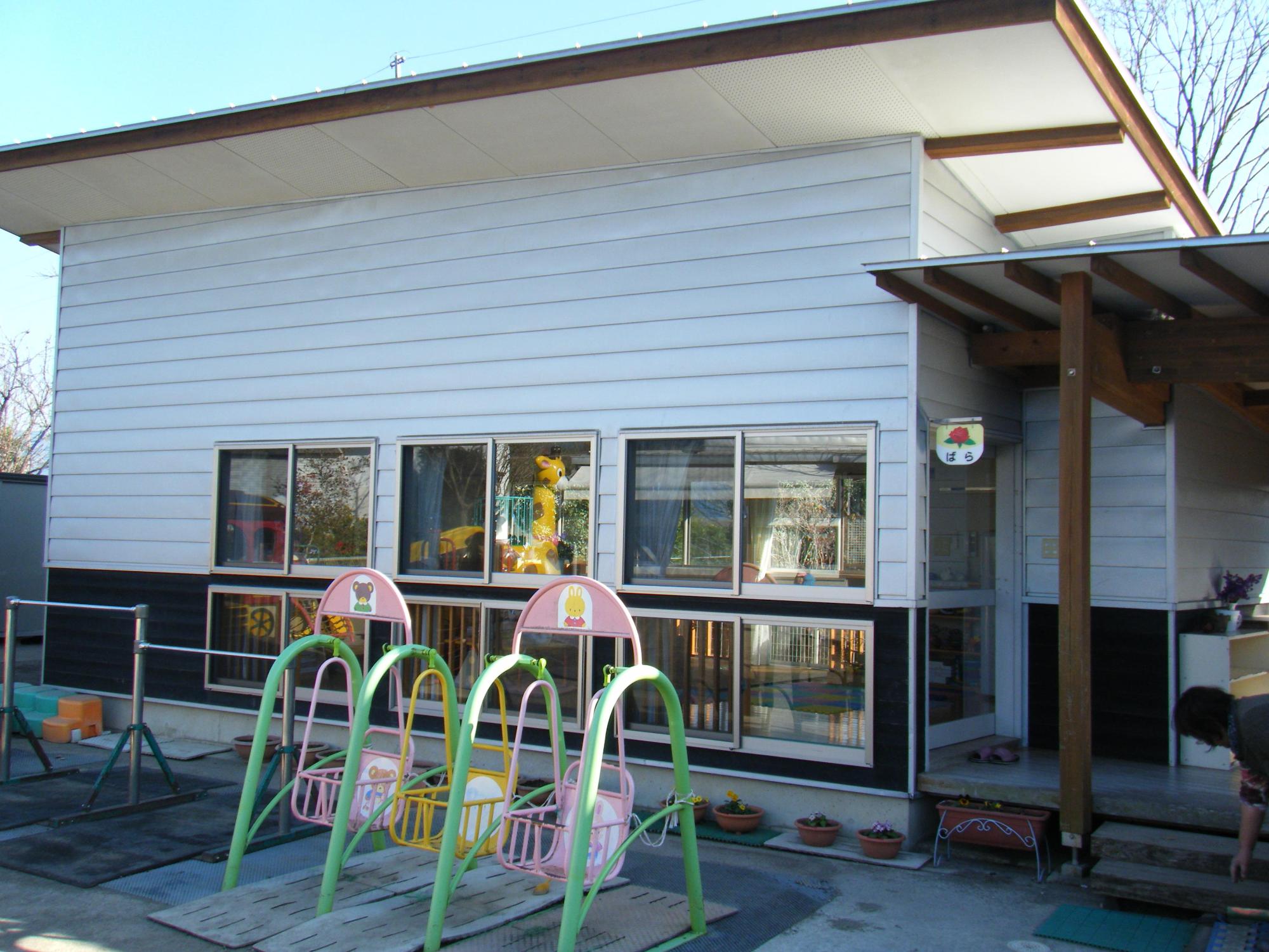 黒肥地保育園子育て支援センターの外観写真。白い建物で、外には鉄棒やブランコなどの遊具が並んでいます。